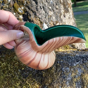 May include: A small, brown and green ceramic jug with a unique, wavy design. The jug has a green glaze on the inside and a brown glaze on the outside.