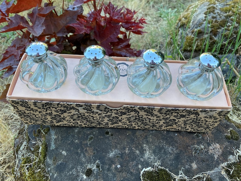 May include: Set of four clear glass salt and pepper shakers with silver tops in a box with a black and white floral pattern.