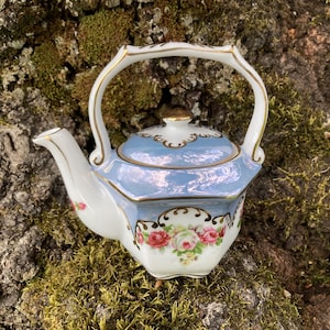 May include: A small, blue and white porcelain teapot with a floral design and gold accents. The teapot has a lid and a handle.