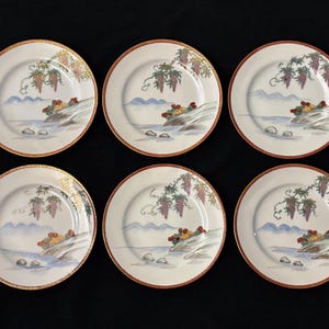 Puede incluir: Seis platos de cerámica blanca con un diseño decorativo. Cada plato presenta una escena de paisaje con uvas, un río y montañas. Los platos tienen un borde dorado y un borde rojo.