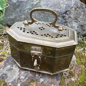 May include: A brass box with a hinged lid and a decorative handle. The box has a geometric pattern of holes and a latch on the front.