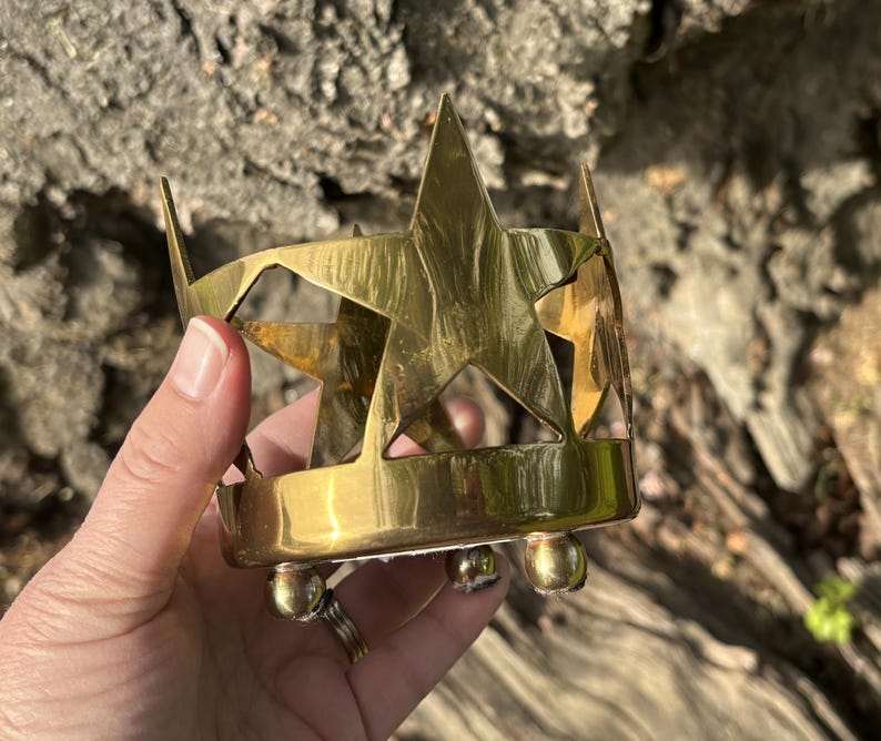 Puede incluir: Un portavelas de lat&oacute;n con dise&ntilde;o de estrella. El soporte tiene forma cil&iacute;ndrica con formas de estrella recortadas y est&aacute; sostenido por tres peque&ntilde;os pies redondos. El lat&oacute;n tiene un tono dorado c&aacute;lido.
