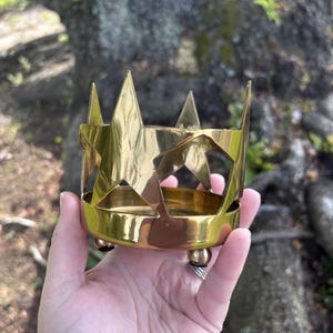 Puede incluir: Un portavelas de metal dorado con un dise&ntilde;o en forma de estrella. El portavelas tiene una base circular con tres peque&ntilde;os pies y una serie de recortes en forma de estrella en los lados. El borde superior presenta acentos en forma de estrella puntiaguda.