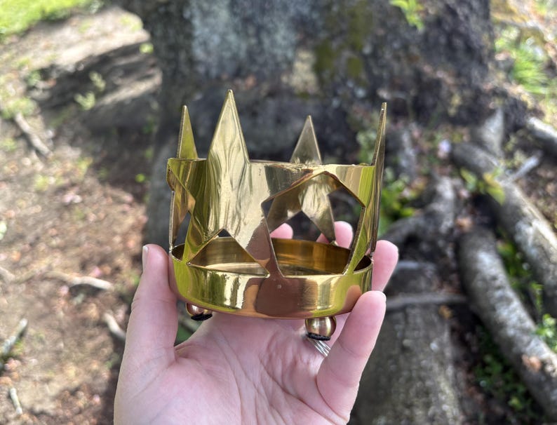 Puede incluir: Un portavelas de metal dorado con un dise&ntilde;o en forma de estrella. El portavelas tiene una base circular con tres peque&ntilde;os pies y una serie de recortes en forma de estrella en los lados. El borde superior presenta acentos en forma de estrella puntiaguda.