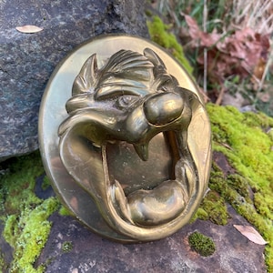 May include: A brass bottle opener shaped like the head of the cartoon character Taz, with a wide open mouth and sharp teeth.