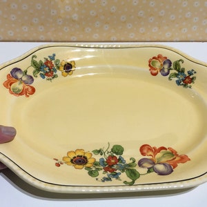 May include: A yellow oval serving platter with a floral design. The flowers are in shades of red, orange, yellow, blue, and purple.