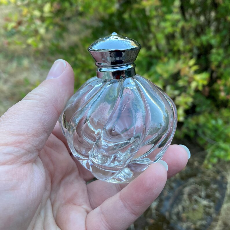 May include: A clear glass bottle with a silver cap. The bottle has a textured, swirling design.