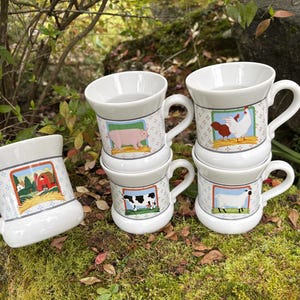 May include: White ceramic mugs with farm animal illustrations. Each mug features a different animal: a pig, cow, sheep, and chicken. The mugs have a handle and a decorative border with a farm scene.