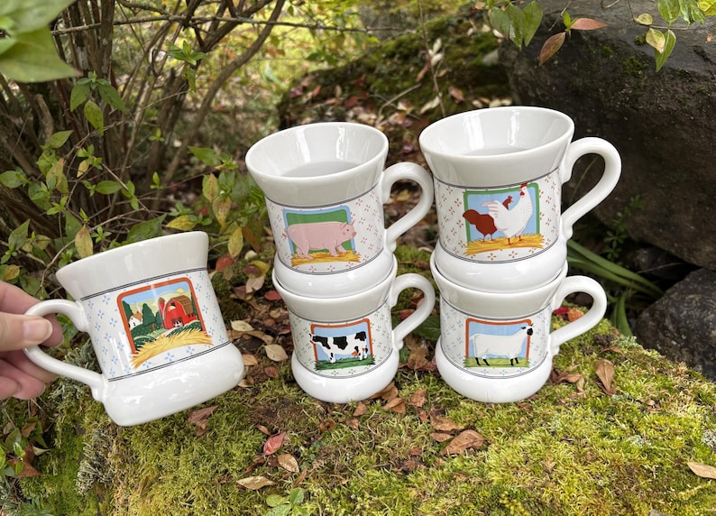May include: White ceramic mugs with farm animal illustrations. Each mug features a different animal: a pig, cow, sheep, and chicken. The mugs have a handle and a decorative border with a farm scene.