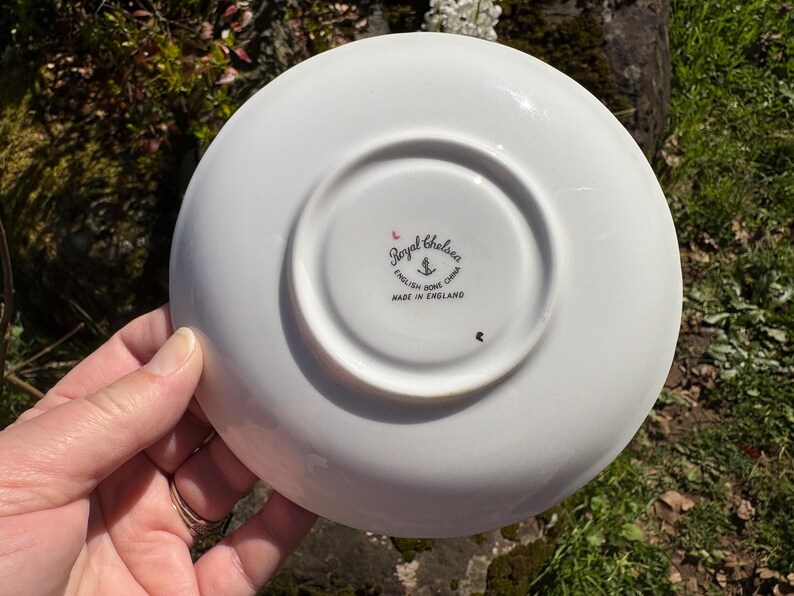 K&ouml;nnte beinhalten: Unterseite einer wei&szlig;en Royal Chelsea English Bone China Untertasse. Die Untertasse hat eine zentrale Vertiefung und einen erh&ouml;hten Rand. Das Royal Chelsea-Logo ist sichtbar, zusammen mit dem Text "MADE IN ENGLAND."