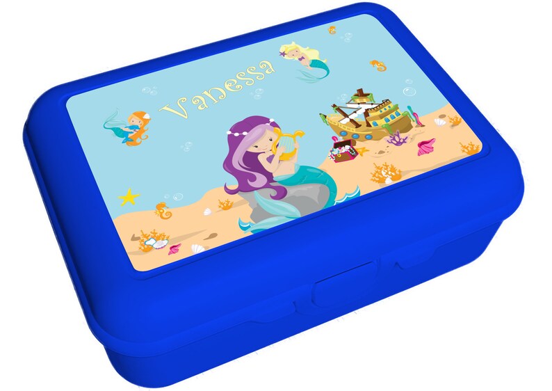 May include: Blue lunchbox with a mermaid theme. The lid features a mermaid with purple hair playing a harp, a ship, and the name "Vanessa".