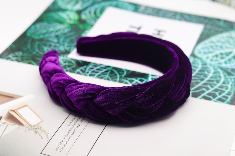 May include: A purple velvet headband with a knotted design. The headband is thick and wide, and it is perfect for adding a touch of elegance to any outfit.