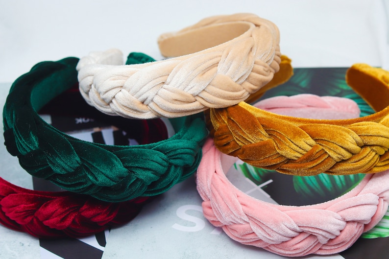 May include: Four braided velvet headbands in different colors: green, beige, mustard yellow, and pink. The headbands are stacked on top of each other.