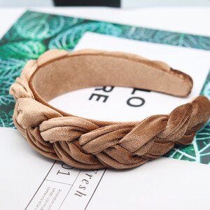May include: A brown velvet headband with a braided knot design. The headband is a simple and stylish accessory for any outfit.