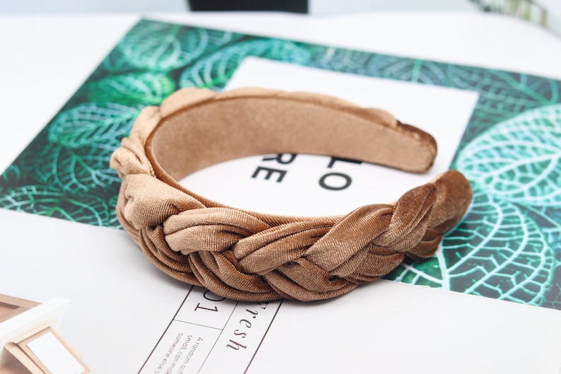 May include: A brown velvet headband with a braided knot design. The headband is a simple and stylish accessory for any outfit.