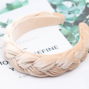 May include: A beige velvet headband with a braided design. The headband is thick and wide, and it is perfect for adding a touch of elegance to any outfit.
