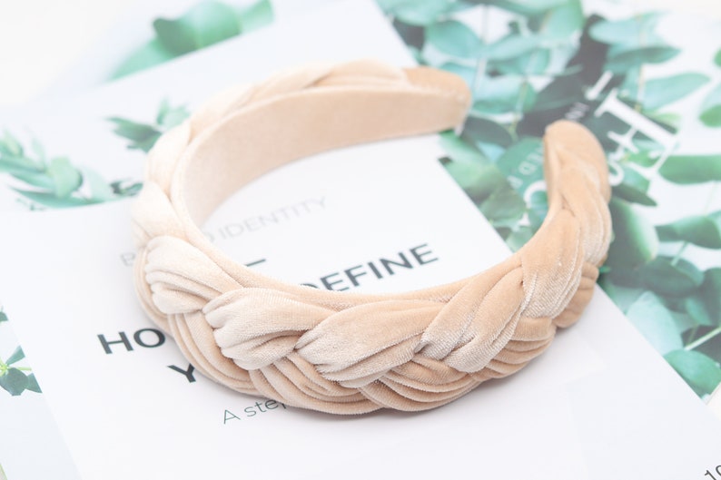 May include: A beige velvet headband with a braided design. The headband is thick and wide, and it is perfect for adding a touch of elegance to any outfit.