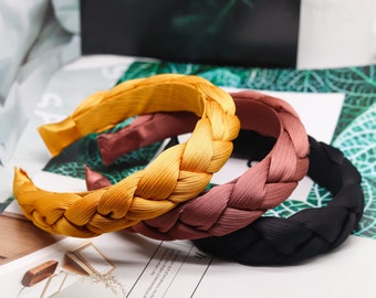 May include: Three braided headbands in yellow, brown and black. The headbands are made of a soft, woven fabric.