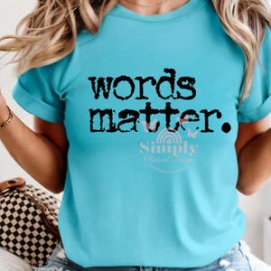 May include: A light blue t-shirt with the words "words matter." in black, block letters. Below the text is the word "Simply" in a script font, with "Obsessed Designs" below it. The shirt has short sleeves.