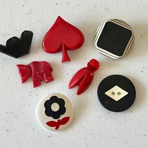 May include: Assortment of six vintage plastic buttons in various shapes and colors.  The buttons include a red spade, a black and white square, a red elephant, a red and white flower, a red bug, and a black button with a white diamond.