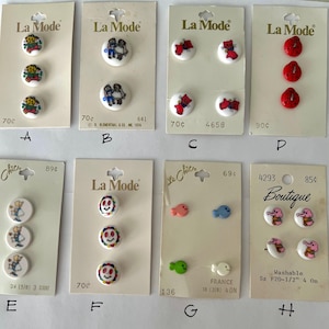 May include: Assortment of colorful buttons with various designs, including children, animals, and smiley faces. The buttons are packaged on white cards with the brand name "La Mode" and "Le Chic" printed on them. The cards also include pricing information and size details.
