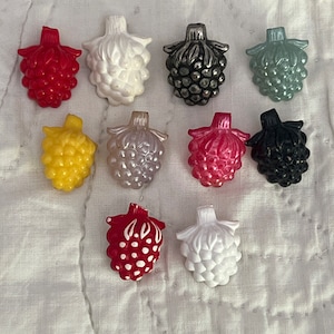 May include: Assortment of 10 grape-shaped buttons in various colors, including red, white, black, yellow, and green. The buttons have a 3D design and are made of plastic.