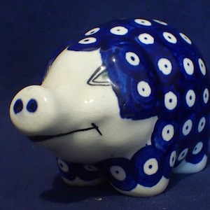 May include: A ceramic pig figurine, primarily white with blue accents. The pig's body is adorned with blue circular patterns, and it has a detailed face with black markings. The figurine is a decorative item.