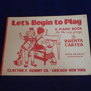 May include: A vintage piano book titled "Let's Begin to Play" with a red illustration of children playing piano. The book is by Buenta Carter and is a rote or note approach for the very young.