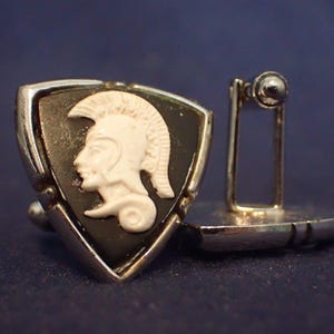 May include: Silver-toned cufflinks with a shield-shaped design. Each cufflink features a black background with a white cameo of a Roman soldier. The cufflinks have a classic, elegant style.
