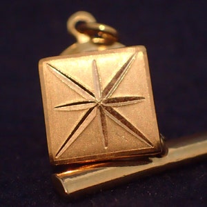 May include: Gold-toned tie tack with a starburst design. The starburst is engraved into the surface of the tie tack.