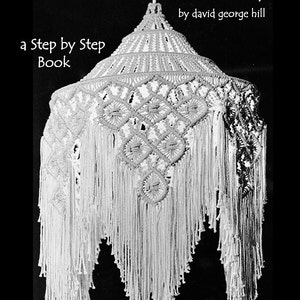 Op de afbeelding: Een witte macramé lampenkap met een geometrisch patroon en lange franjes. De omslag van het boek luidt "How To Make a Macrame Lamp" en "a Step by Step Book" met de naam van de auteur "by david george hill". De titel van het boek luidt ook "Book 1: Wire Frame".
