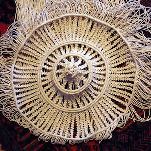 K&ouml;nnte beinhalten: Ein wei&szlig;es geh&auml;keltes Mandala mit einem Fransenrand. Das Mandala besteht aus einer Reihe konzentrischer Kreise mit einem Mittelpunkt.