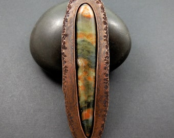 May include: A copper pendant with a hammered finish and a long, oval-shaped stone with green, brown, and orange colors.