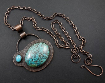 May include: A copper necklace with a turquoise pendant. The pendant features a large oval turquoise stone surrounded by a smaller round turquoise stone. The chain is a simple copper chain.