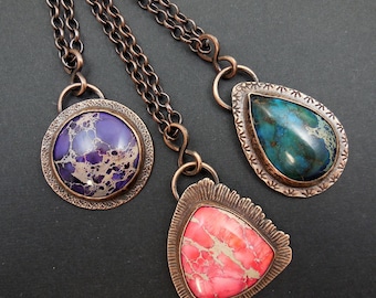 May include: Three copper necklaces with different shaped pendants featuring colorful, marbled, stone-like inserts. The pendants are a round, teardrop, and a triangle shape.