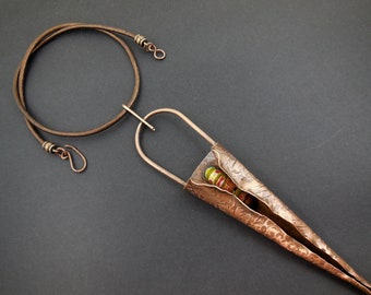 May include: A copper necklace with a textured, leaf-shaped pendant. The pendant has a small opening that reveals colorful glass beads.