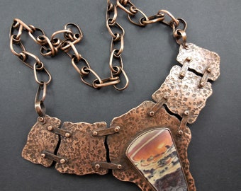 May include: A copper necklace with a large, irregularly shaped agate stone pendant. The necklace has a hammered copper chain and a chunky, textured copper design.