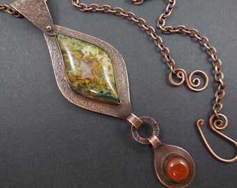 May include: A copper necklace with a large green and brown agate stone pendant and a smaller carnelian stone pendant. The necklace has a chain with a hammered texture.