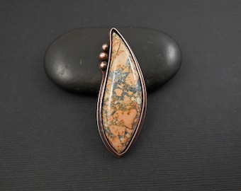 May include: A copper pendant with a teardrop-shaped, orange, gray, and black stone set in a copper frame.