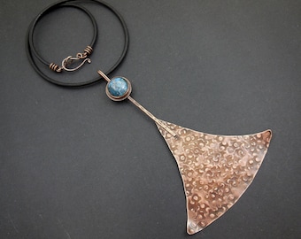 May include: A copper necklace with a blue stone pendant and a textured copper triangle pendant. The necklace is on a black cord.