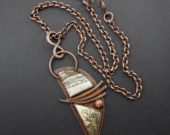 May include: A copper necklace with a pendant featuring a green and white agate stone set in a copper frame. The pendant has a geometric design with two curved lines and a small copper bead.