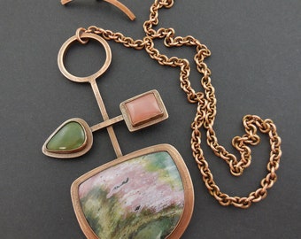 May include: A copper necklace with a geometric pendant featuring a pink and green stone, a smaller green stone, and a pink stone. The necklace has a copper chain.