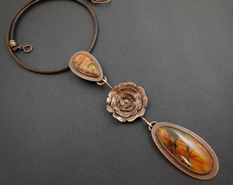 May include: A copper necklace with a rose-shaped pendant and two teardrop-shaped stones with a marbled pattern in shades of brown, orange, and yellow.