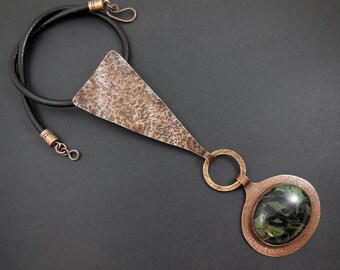 May include: A copper necklace with a hammered triangular pendant and a green and black stone pendant. The necklace is on a black leather cord.