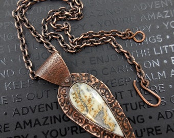 May include: A copper necklace with a pendant featuring a white and brown agate stone. The pendant is shaped like a teardrop and has a textured copper frame. The chain is made of copper and has a lobster clasp.