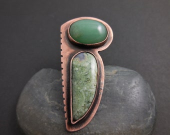 May include: A copper pendant with two green stones set in it. The larger stone is round and the smaller stone is a teardrop shape.