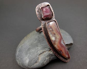 May include: A copper ring with a pink and white agate stone set in a textured copper bezel. The ring is designed in a long, pointed shape.