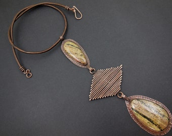 May include: A copper necklace with a geometric pendant and two oval-shaped stones. The stones are a light brown with green and black streaks.