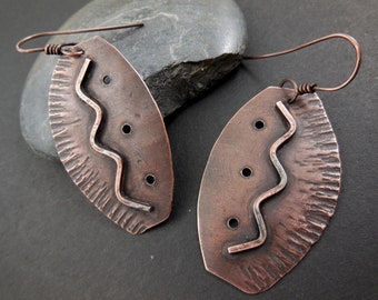 May include: A pair of copper earrings with a textured, hammered finish. Each earring features a wavy line design and four small holes. The earrings are attached to a simple wire hook.