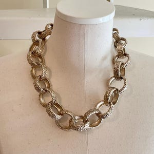 Puede incluir: Un collar dorado con eslabones texturizados grandes. La cadena gruesa se exhibe en un maniqu&iacute;, mostrando su dise&ntilde;o audaz. El collar es una pieza de joyer&iacute;a llamativa.